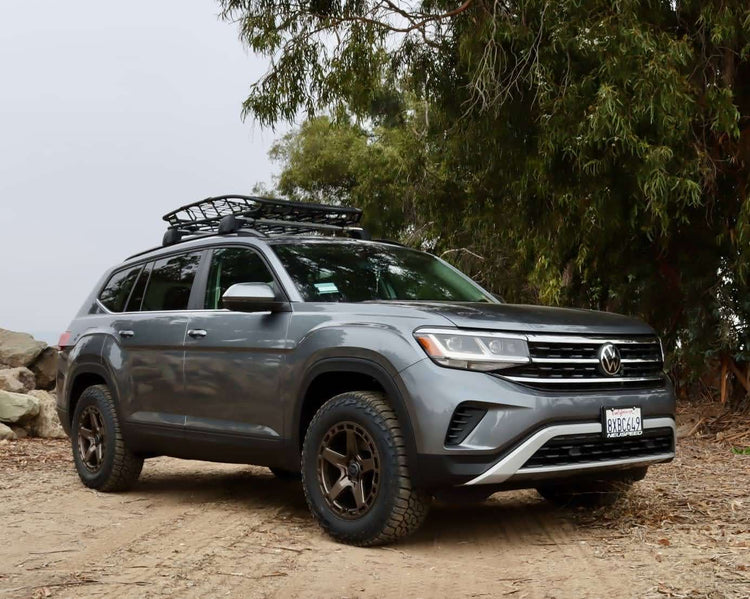 VW Atlas outfitted with lift kit, skid plates, and roof rack parked on rocky off-road trail with dirt and gear in view