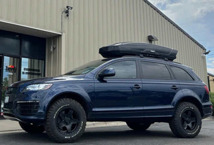 Lifted Audi Q7 with trail lighting, roof rack, and skid plates parked on rocky mountain trail