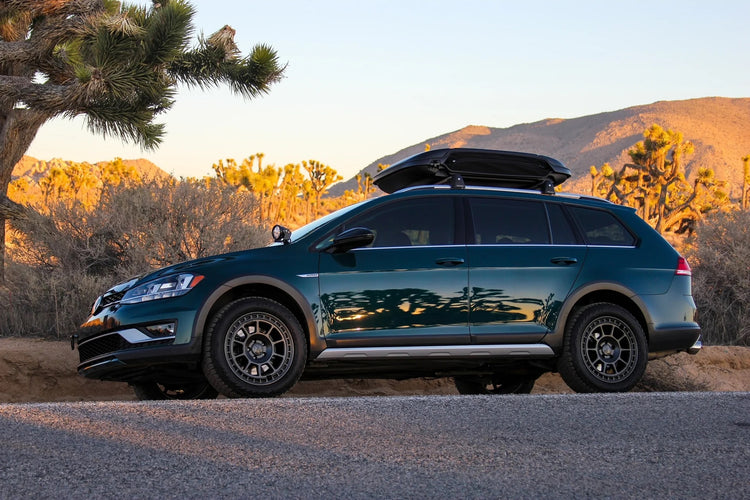 Lifted VW MK7 Alltrack with skid plates and roof rack parked on dirt road with trail dust and gear loaded