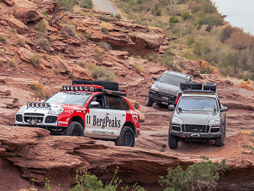 Lifted Porsche Cayenne outfitted with off-road bumpers, wheels, and skid plates parked on a rocky Colorado trail